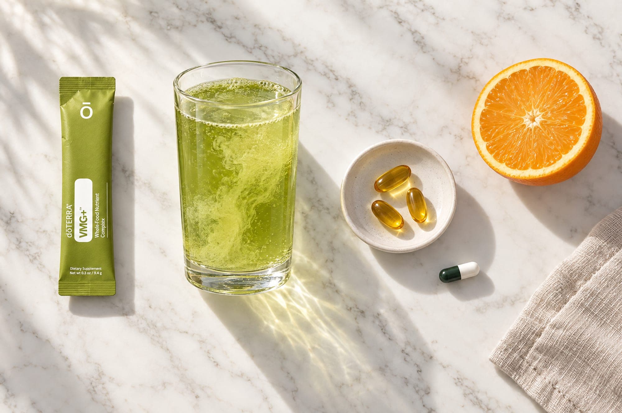 Overhead view of the three doses on marble: a VMG+ stick, the green drink in a glass, three softgels on a dish, one capsule, and a halved orange